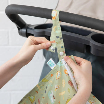 Hands attach a Bumkins Wet Bag: Camp Gear to a stroller handle using the snap button closure on the strap.