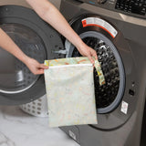 A person holds Bumkins Wet Bag: Camp Gear in front of an open front-loading washing machine.