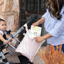 Load image into Gallery viewer, A woman places a book into a Bumkins Wet Bag: Lace attached to a stroller with a child outdoors.

