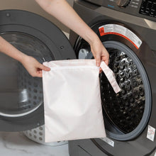 Load image into Gallery viewer, A person holds Bumkins Wet Bag: Lace in front of an open front-loading washing machine.

