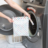 A person holds Bumkins Wet Bag: Mickey & Friends Varsity in front of an open front-loading washing machine.