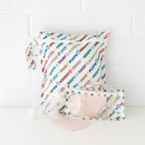 Bumkins Wet Bag: Mickey & Friends Varsity sits on a white table against a white brick wall, with breast pump parts in front. 