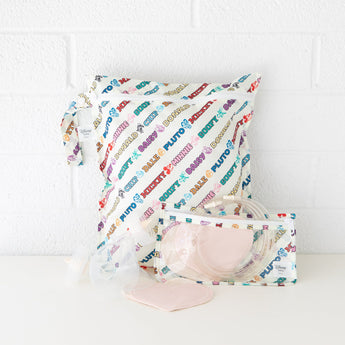 Bumkins Wet Bag: Mickey & Friends Varsity sits on a white table against a white brick wall, with breast pump parts in front. 