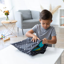 Load image into Gallery viewer, A child in a gray shirt opens a Bumkins Wet Bag: Mickey Mouse Icon Black + White at a white table in a living room with toys and flowers.
