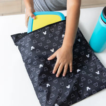 Load image into Gallery viewer, Close-up of a child placing a yellow container in a Bumkins Wet Bag: Mickey Mouse Icon Black + White next to a blue water bottle on a table.
