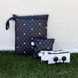 Bumkins Wet Bag: Mickey Mouse Icon Black + White sits on grass against a beige textured wall with three other bags.