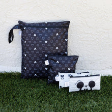 Load image into Gallery viewer, Bumkins Wet Bag: Mickey Mouse Icon Black + White sits on grass against a beige textured wall with three other bags.
