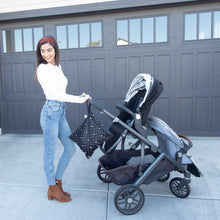 Load image into Gallery viewer, A person in a white sweater pushes a stroller by a garage, with a Bumkins Wet Bag: Mickey Mouse Icon Black + White attached to the handle.
