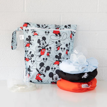 Bumkins Wet Bag: Mickey Mouse Classic sits on a white table against a white brick wall with cloth diapers and breast pump parts in front.