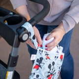 A person places a towel in a Bumkins Wet Bag: Mickey Mouse Classic hanging from a stroller handle.