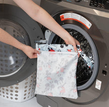 Load image into Gallery viewer, A person holds Bumkins Wet Bag: Mickey Mouse Classic in front of an open front-loading washing machine.

