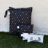 Bumkins Wet Bag: Minnie Mouse Icon Black + White sits on grass against a beige textured wall with three smaller bags.