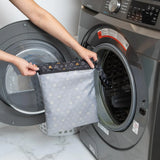 A person holds Bumkins Wet Bag: Minnie Mouse Icon Black + White in front of an open front-loading washing machine.