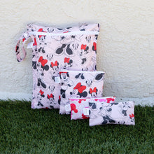 Load image into Gallery viewer, Bumkins Wet Bag: Minnie Mouse Classic sits by smaller, similarly printed pouches on grass against a beige textured wall.
