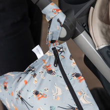 Load image into Gallery viewer, Close-up of a stroller with Bumkins Wet Bag: No Tricks, Just Treats, featuring Halloween ghosts and pumpkins, hanging from the handle.
