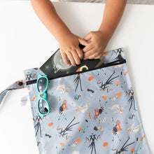 Load image into Gallery viewer, A child slips a book into a Bumkins Wet Bag: No Tricks, Just Treats on a white table, with blue sunglasses nearby.

