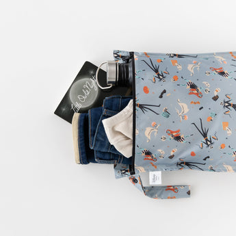 Bumkins Wet Bag: No Tricks, Just Treats holds a book, water bottle, blue jeans, and a light shirt on a white background.