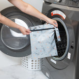 A person holds a Bumkins Wet Bag: No Tricks, Just Treats in front of a front-loading washing machine.