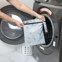 Load image into Gallery viewer, A person holds a Bumkins Wet Bag: No Tricks, Just Treats in front of a front-loading washing machine.
