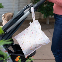 Load image into Gallery viewer, A person in jeans pushes a baby in a stroller outdoors, with Bumkins Wet Bag: Princess Magic hanging from the handle.

