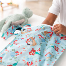 Load image into Gallery viewer, A child places items into a Bumkins Wet Bag: Disney Princess Ariel, with mermaid illustrations; a plush toy sits on the white table.
