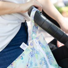 Load image into Gallery viewer, Close-up of a person pushing a stroller with a Bumkins Wet Bag: Aloha Stitch hanging from the handle.
