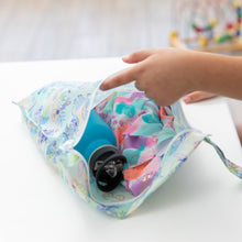 Load image into Gallery viewer, A hand reaches into Bumkins Wet Bag: Aloha Stitch, revealing a teal bottle and vibrant fabric on a pristine white table.
