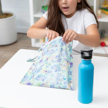 Load image into Gallery viewer, A child opens the Bumkins Wet Bag: Aloha Stitch at a table next to a blue water bottle, highlighting its reusable features.
