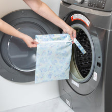 Load image into Gallery viewer, A person holds a Bumkins Wet Bag: Aloha Stitch in front of an open front-loading washing machine.
