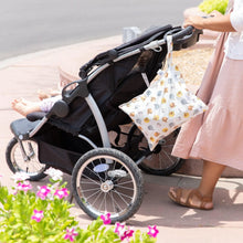 Load image into Gallery viewer, A person pushes a stroller on a sunny day with Bumkins Wet Bag: Winnie and Friends hanging from the handle, pink flowers nearby.
