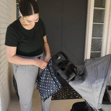 Load image into Gallery viewer, A woman in green top and gray pants zips a Bumkins Wet Bag: Super Mario™ Lineup attached to a stroller in front of a door.
