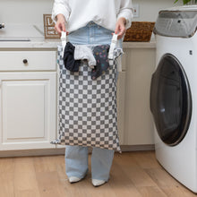 Load image into Gallery viewer, In a laundry room, a person holds a Bumkins Extra Large Wet Bag: Charcoal Check filled with clothes near a washing machine.

