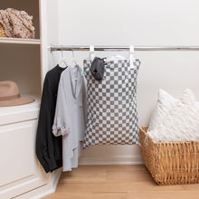 Load image into Gallery viewer, A closet corner with shirts and a Bumkins Extra Large Wet Bag: Charcoal Check hanging on a rod, a basket with pillows, and a hat on shelf.
