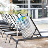 Bumkins Extra Large Wet Bag: Charcoal Check hangs on a poolside lounge chair with sunglasses and swimwear; nearby are chairs and umbrellas.