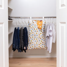Load image into Gallery viewer, An organized closet with jeans, shirts, and a Bumkins Extra Large Wet Bag: Winnie + Friends with white walls and light wood floors.
