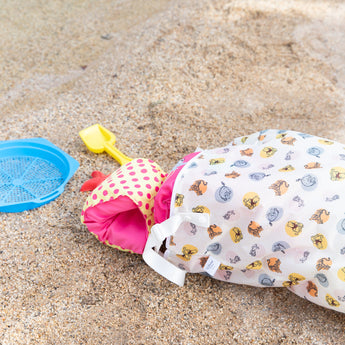 Beach toys spill out of a Bumkins Extra Large Wet Bag: Winnie + Friends laying on the sand.
