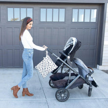 Load image into Gallery viewer, A woman wearing jeans &amp; a white top pushes a double stroller with a Bumkins Wet/Dry Bag: Hearts attached to the handle in front of a garage.
