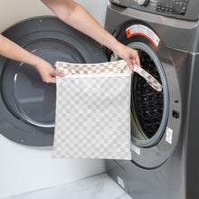 Load image into Gallery viewer, A person holds Bumkins Wet/Dry Bag: Sand Check in front of an open front-loading washing machine.
