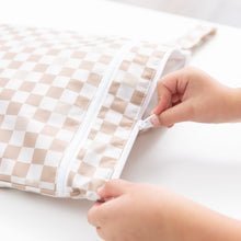 Load image into Gallery viewer, Hands zipping a Bumkins Wet/Dry Bag: Sand Check on a white table.
