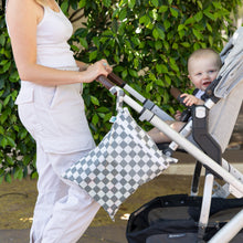 Load image into Gallery viewer, A person in a white outfit pushes a baby in a stroller with Bumkins Wet/Dry Bag: Charcoal Check attached. Green foliage in the background.
