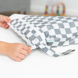 Hands zip a Bumkins Wet/Dry Bag: Charcoal Check on a white table.