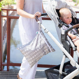 A woman pushes a stroller with a child and a Bumkins Wet/Dry Bag: Lunar Phase hanging from the handle near the waterfront.