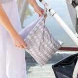 A person opens a Bumkins Wet/Dry Bag: Lunar Phase attached to a stroller handle on a bridge, ideal for keeping essentials organized on the go.