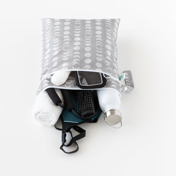 Bumkins Wet/Dry Bag: Lunar Phase lays on a white background, filled with gym essentials like clothes, a towel, a phone, and a water bottle.