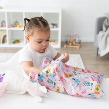 Load image into Gallery viewer, A girl reaches into a Bumkins Wet/Dry Bag: Boots at a white table next to a stuffed unicorn; toy filled shelves behind.
