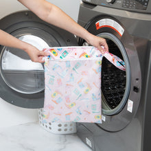 Load image into Gallery viewer, A person holds a Bumkins Wet/Dry Bag: Boots in front of a front-loading washing machine.
