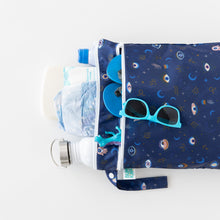 Load image into Gallery viewer, Bumkins Wet/Dry Bag: Evil Eye holds diapers, bottles, wipes &amp; teal sunglasses on a white background.

