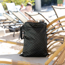 Load image into Gallery viewer, Roamio by Bumkins Wet/Dry Bag: Rich Black holds shoes and a water bottle on a rattan chair with lounge chairs in the background.

