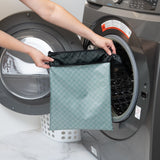 A person holds Roamio by Bumkins Wet/Dry Bag: Rich Black  in front of an open front-loading washing machine.