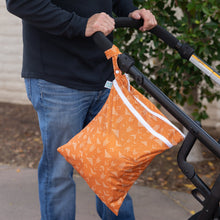 Load image into Gallery viewer, A person strolls outdoors with a Bumkins Wet/Dry Bag: Grounded, featuring zippered compartments, hanging from the stroller handle.
